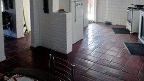 A kitchen with white cabinets, a refrigerator, a stove, and a window. - Suítes Rolim (Arraial do Cabo)