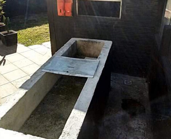 A concrete structure with a rectangular opening, possibly a well or a sink, surrounded by a tiled patio area. - Suítes Rolim (Arraial do Cabo)