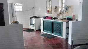 A compact kitchen with a stove, a sink, and a window. - Suítes Rolim (Arraial do Cabo)