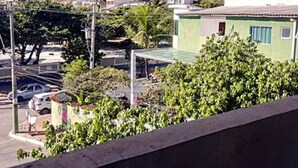 A view of a residential area with a green building, a street, and a hill in the background. - Suítes Rolim (Arraial do Cabo)