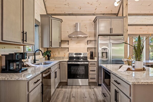 Une cuisine moderne dotée de plans de travail en granit, d’appareils électroménagers en acier inoxydable et de meubles en bois.