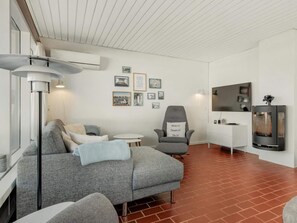 A modern living room with a grey sofa, a grey armchair, a small round table, and a flat-screen TV mounted on the wall. - 5 Star Holiday Home in Pandrup (Pandrup)
