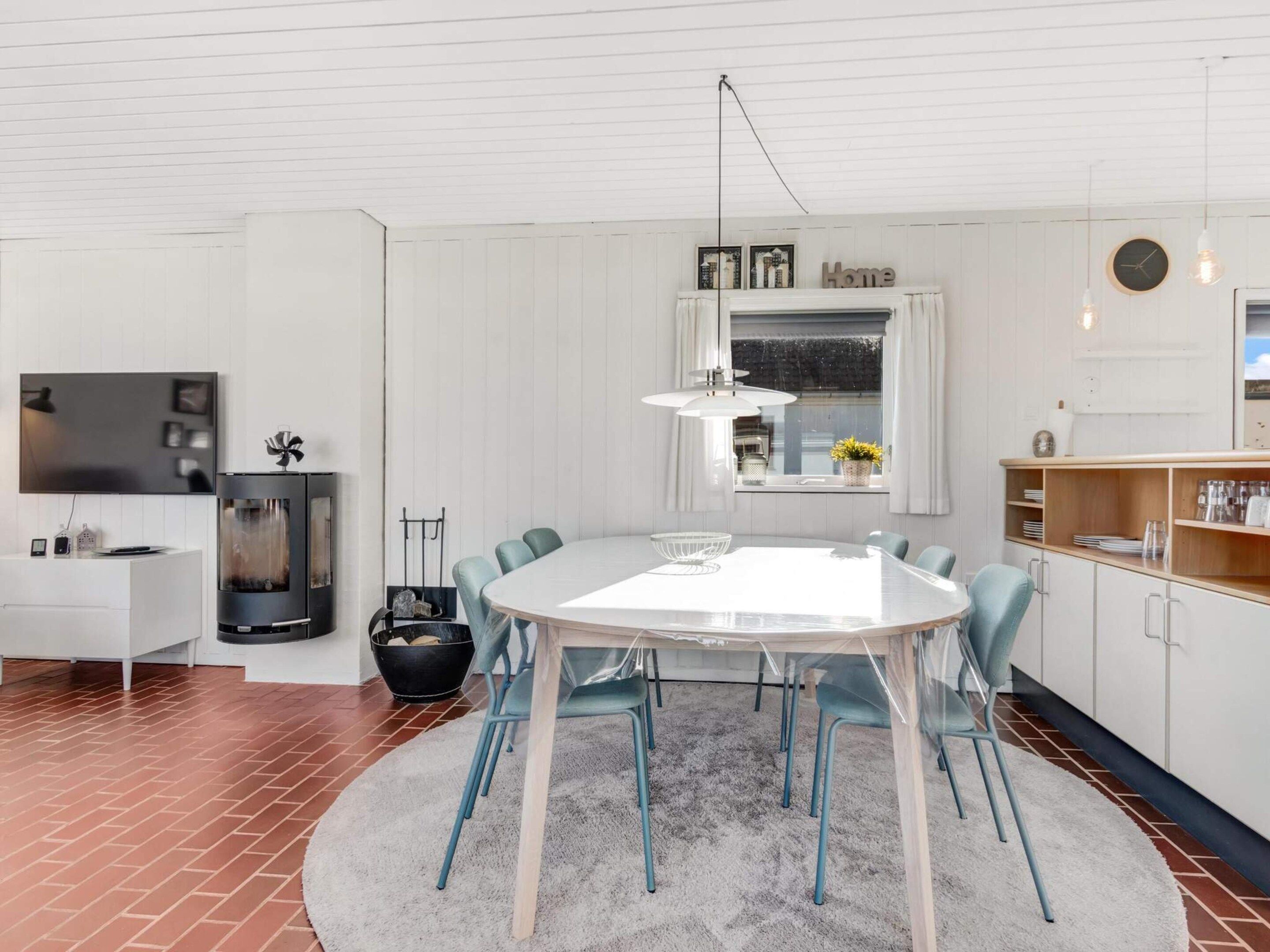 A modern kitchen with a round dining table, chairs, a built-in stove, and a window with curtains.