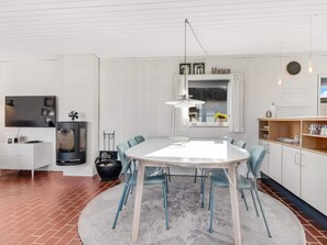 A modern kitchen with a round dining table, chairs, a built-in stove, and a window with curtains. - 5 Star Holiday Home in Pandrup (Pandrup)