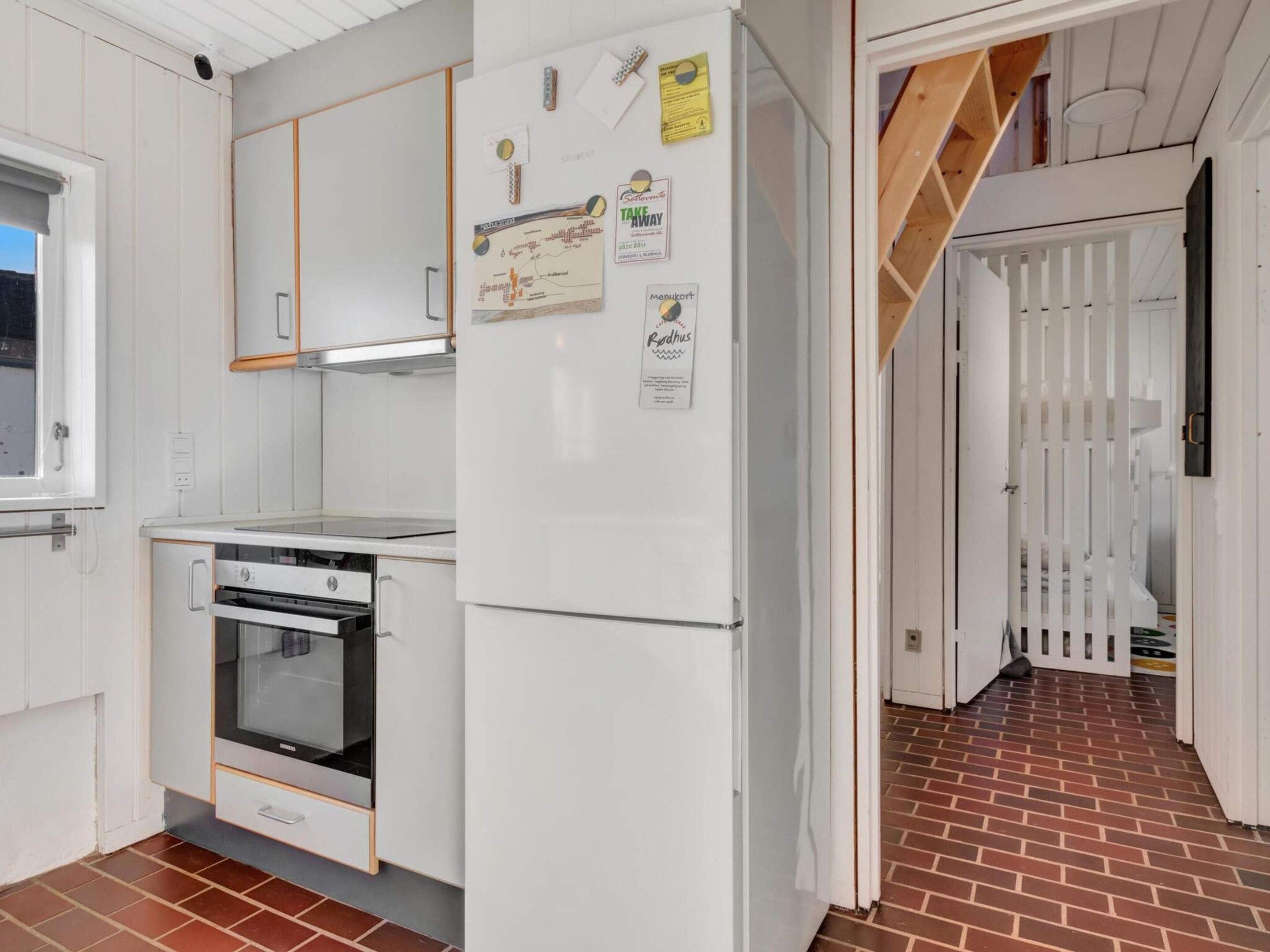 A kitchen with white cabinets, a refrigerator, and a built-in oven. There are various notes and a map on the wall.