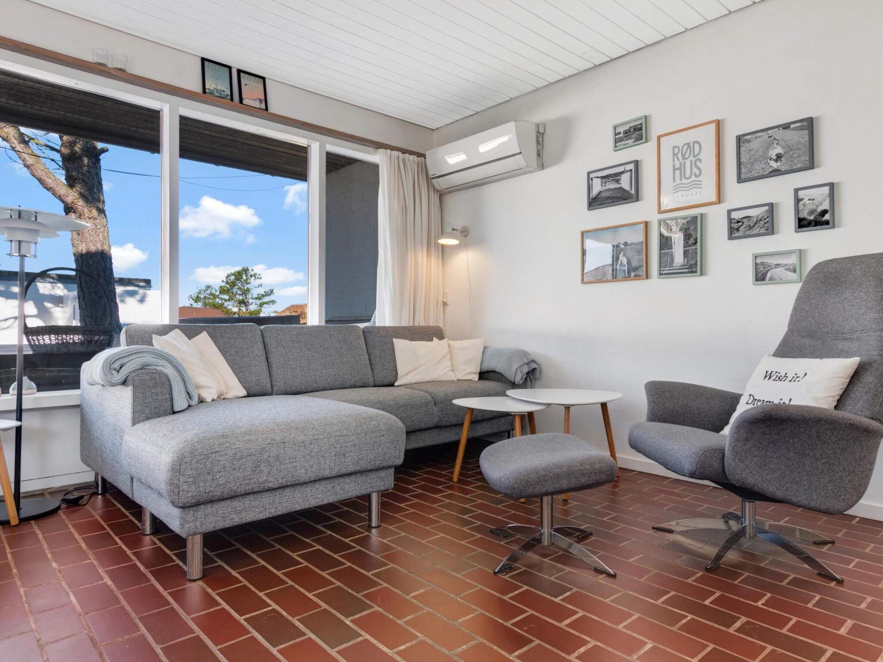Un salon moderne avec un canapé gris, une table basse ronde et un fauteuil gris. Plusieurs tableaux encadrés ornent le mur.