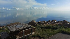 A calm lake with a wooden bench and rocks in the foreground. - 2 Person Holiday Home in Ringkobing (Ringkobing)