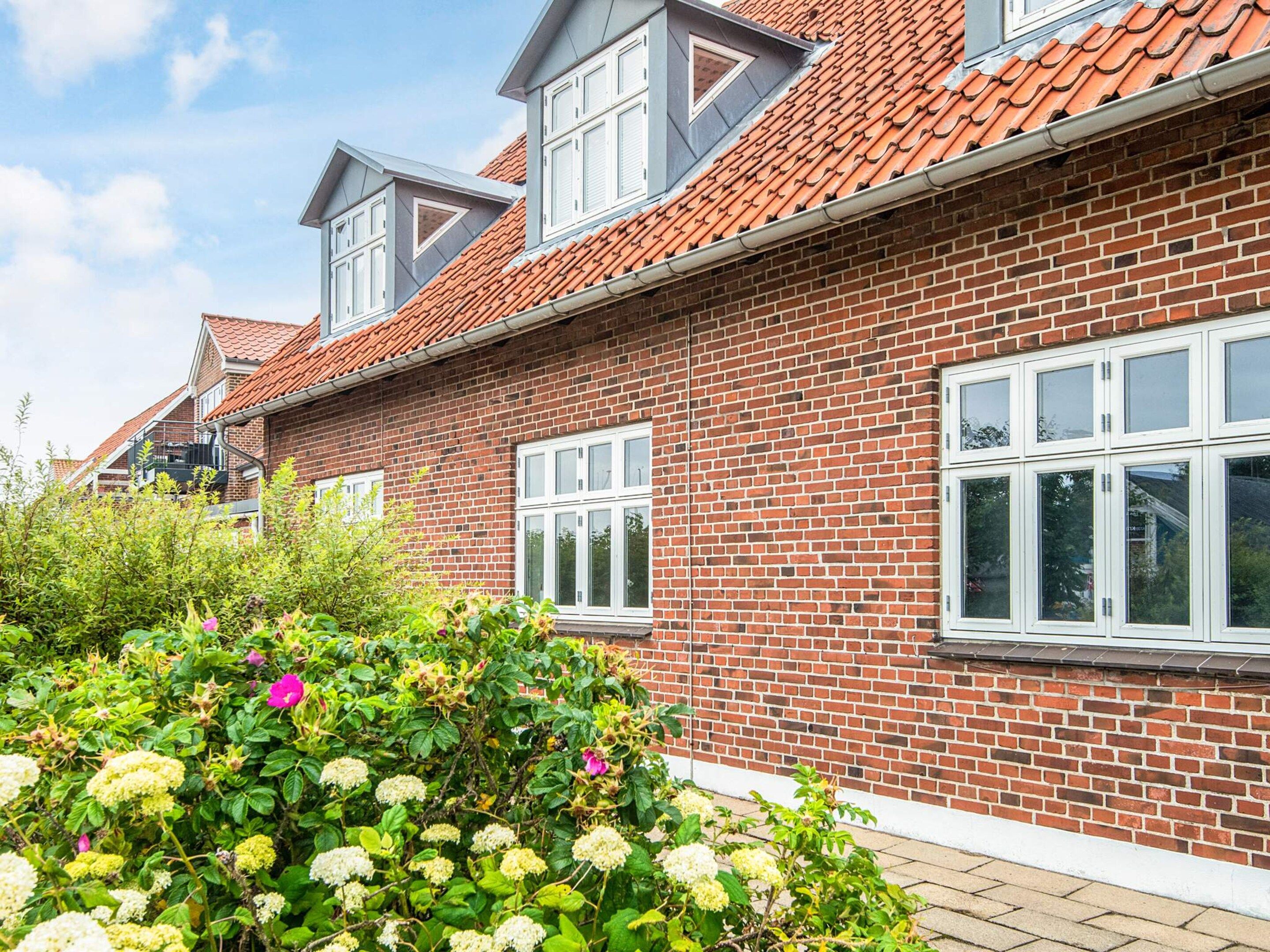 A brick house with a red-tiled roof, white windows, and a garden with hydrangea flowers.