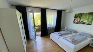 Un dormitorio con dos camas, un ventanal corredizo que da a un balcón, una silla blanca y una lámpara de pared.