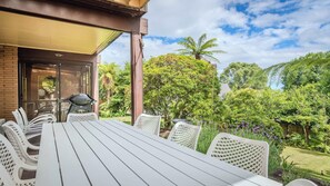 A covered outdoor dining area with a table and chairs, a grill, and a view of a lush garden with various trees and plants. - Highfield on High - Spa Pool, Walk to Redwoods (Rotorua)