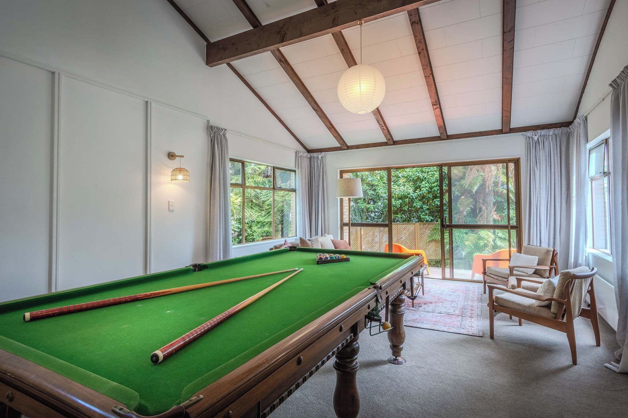 A pool table in a room with large windows, wooden beams, and a hanging light fixture.