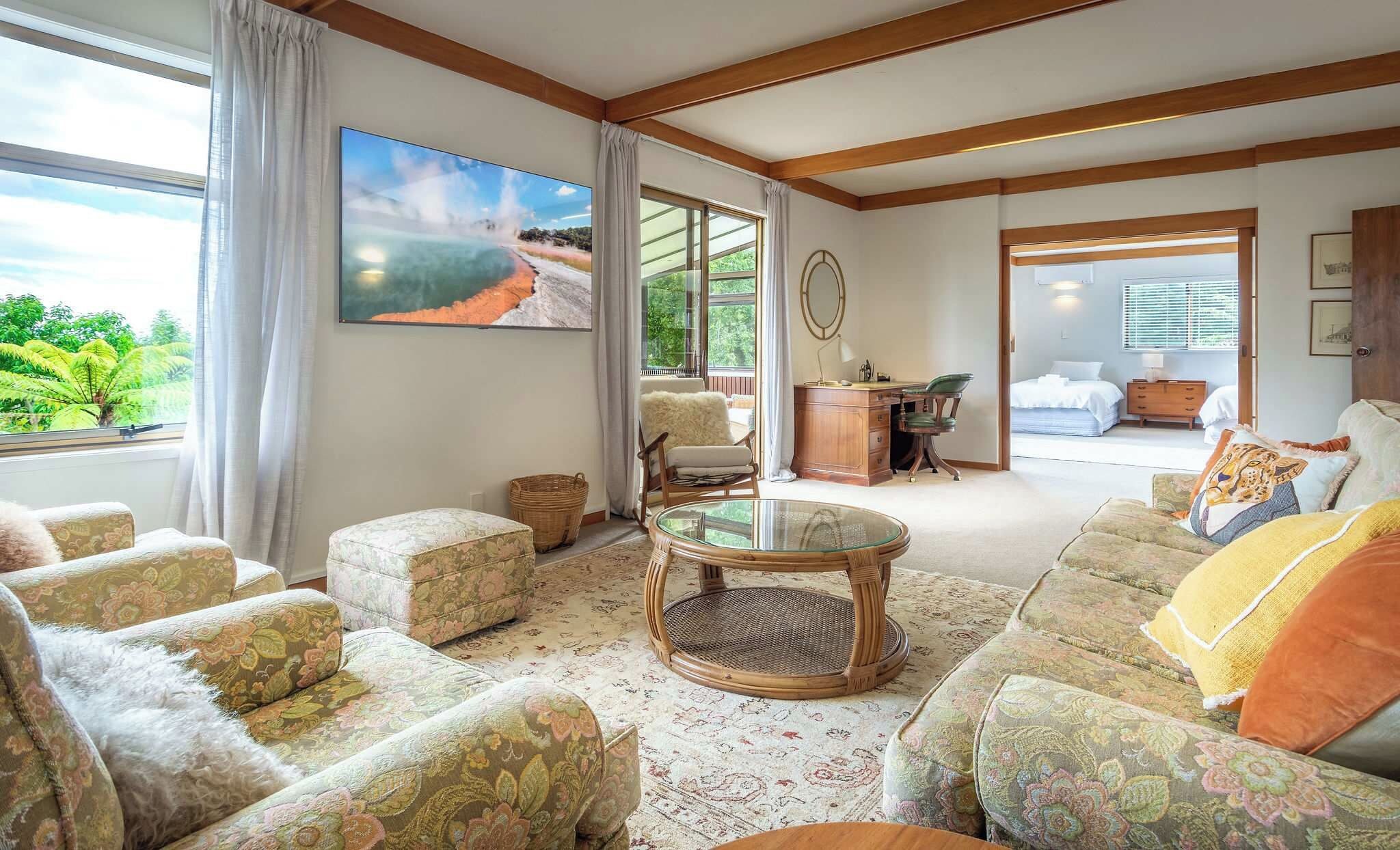 A spacious living room with a large window, a comfortable sofa set, a wooden coffee table, and a painting of a natural landscape.