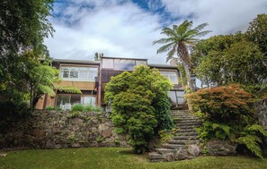 A two-story house with a stone wall, a large tree, and a staircase leading to the upper level. - Highfield on High - Spa Pool, Walk to Redwoods (Rotorua)