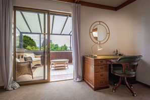 A room with a sliding glass door leading to an outdoor patio area, a wooden desk with drawers, a green upholstered chair, and a wall-mounted mirror.