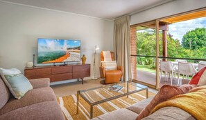 A modern living room with a large flat-screen TV, a leather armchair, a glass coffee table, and a sofa.