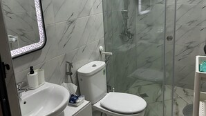 A bathroom with a glass-enclosed shower, a sink, a toilet, and a mirror with lights. - 154 av al manbat martil  (Martil)