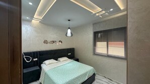 A bedroom with a bed, a bedside table, a wall-mounted lamp, a window with blinds, and a ceiling with recessed lighting. - 154 av al manbat martil  (Martil)