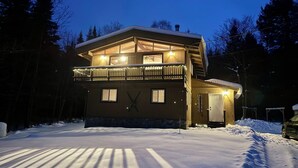 Eine zweistöckige Holzhütte mit Balkon, umgeben von Schnee und Bäumen.