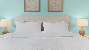 Una cama bien tendida con sábanas blancas, dos cuadros enmarcados y dos lámparas de noche a cada lado.