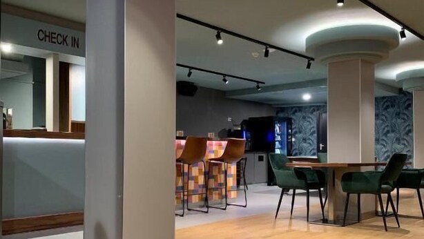 A modern interior with a check-in counter, wooden flooring, and green chairs around a table. - Hostel The Globe (Amsterdam)