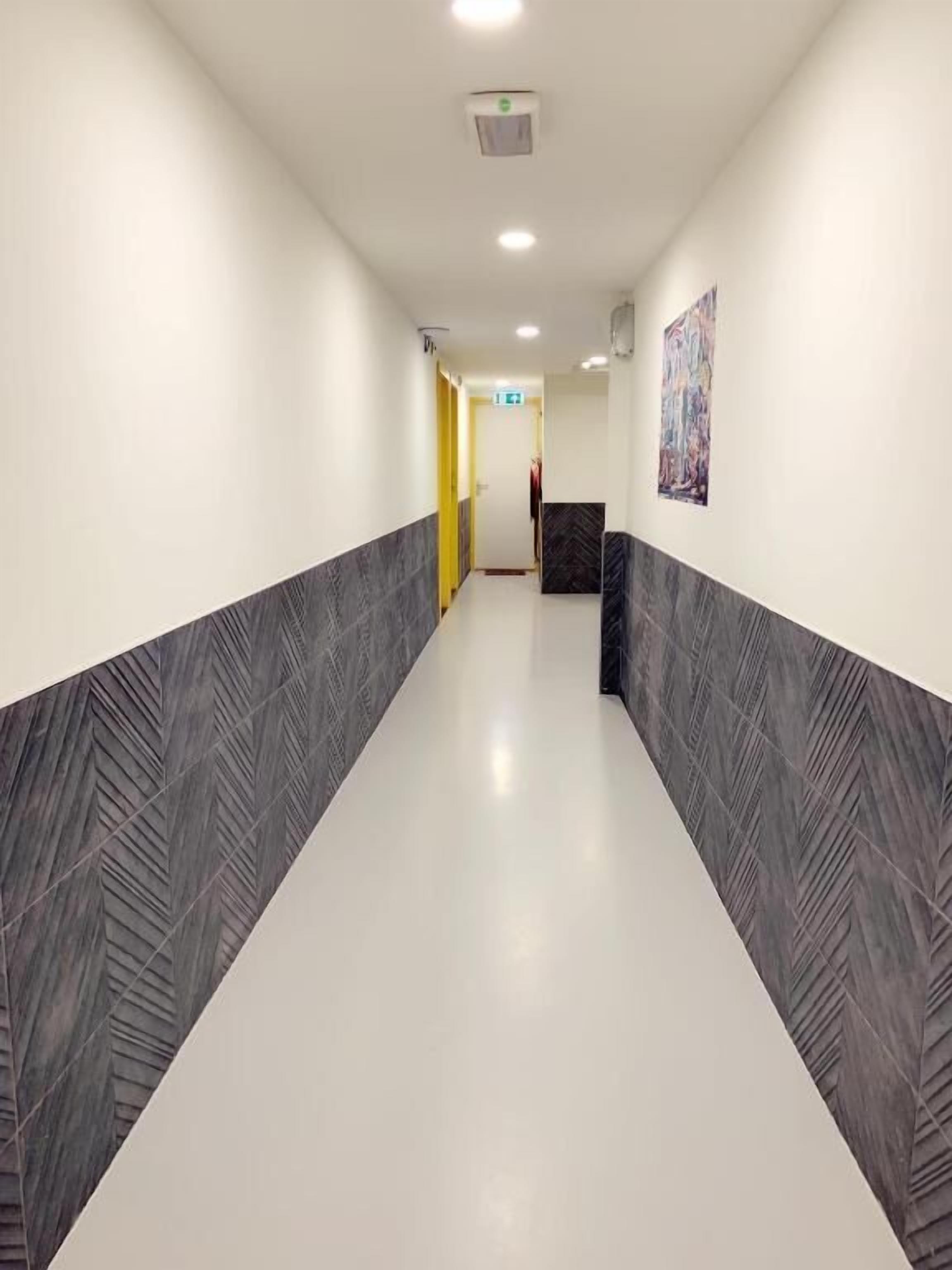 A hallway with a white floor and grey patterned walls, leading to a reception area with a painting on the wall.