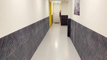 A hallway with a white floor and grey patterned walls, leading to a reception area with a painting on the wall.