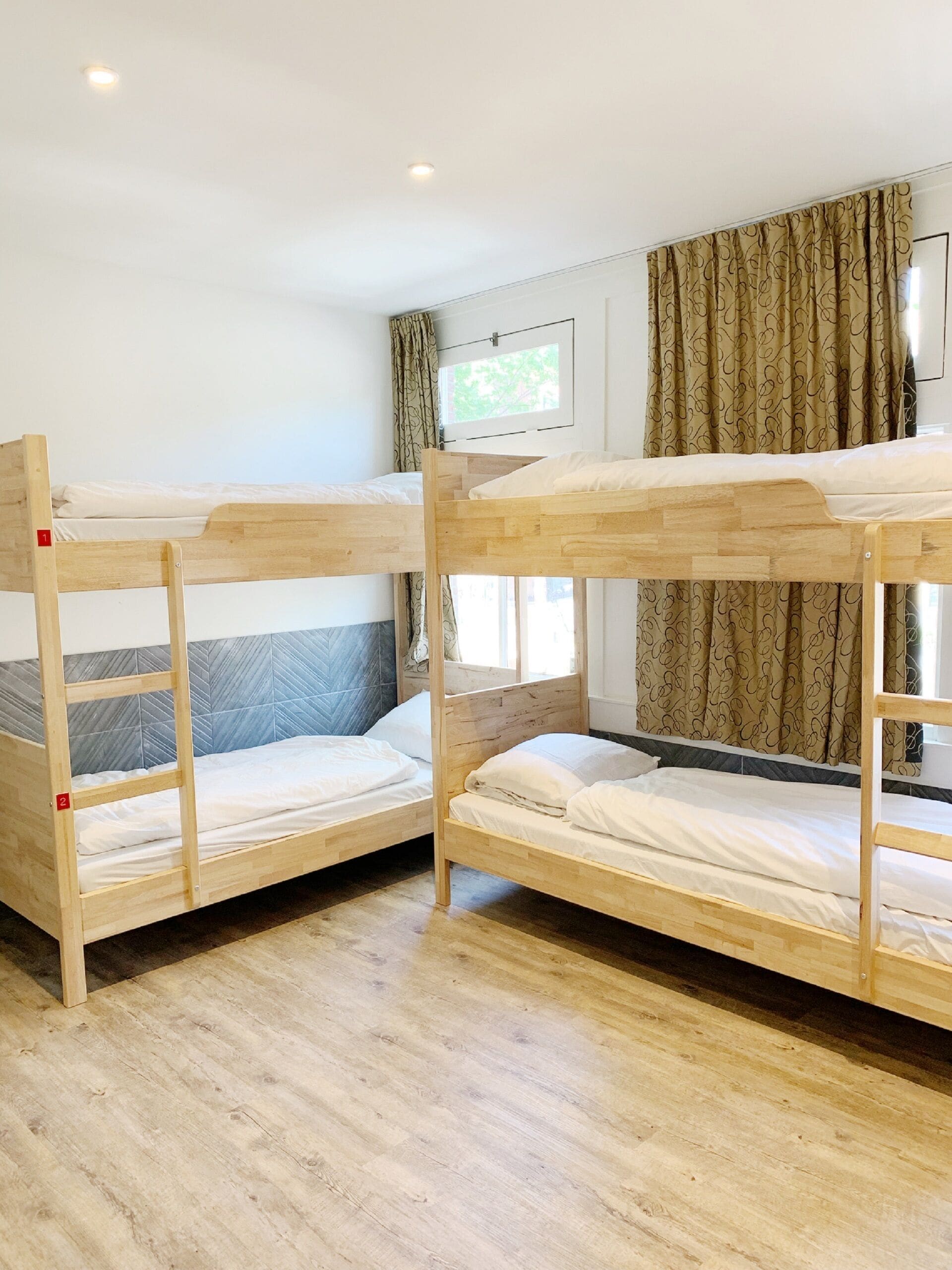 A room with two bunk beds, a window with curtains, and a wooden floor.