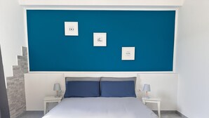 Une chambre à coucher avec un grand lit, deux tables de chevet et un mur d’accent bleu orné de tableaux encadrés.