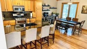 A kitchen with wooden cabinets, a stainless steel stove, and a dining area with a wooden table and chairs.