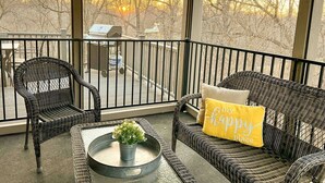 A balcony with wicker furniture, a grill, and a view of trees.