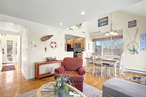A spacious living area with a red armchair, a dining table with chairs, and a kitchen in the background.