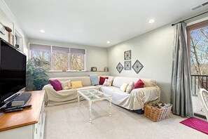 A living room with a sofa, a glass coffee table, a TV, and a window with blinds.