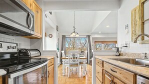 A kitchen with wooden cabinets, a stainless steel sink, and a dining area with a table and chairs. - Amazing Lake Views! Close to Resort! Patio, Fireplace & Dog Friendly! (Galena)