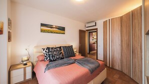 A bedroom with a bed, bedside tables, a nightstand, a wall-mounted air conditioner, and a door leading to a bathroom. - Casa Gioia - Relaxation between Riccione, Rimini, and San Marino (Emilia-Romagna)