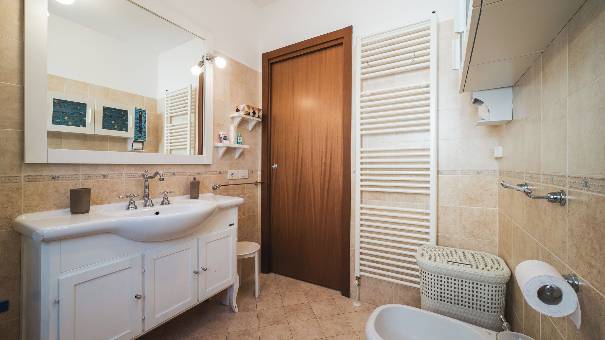 A bathroom with a wooden door, a white sink with two faucets, a mirror, and a toilet.