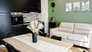 A modern kitchen with black cabinets, a wooden dining table, and a beige sofa in a living area with green walls and artwork. - Holiday home catania 5km from the center relaxation apartment complete kitchen
 (Sicilia)