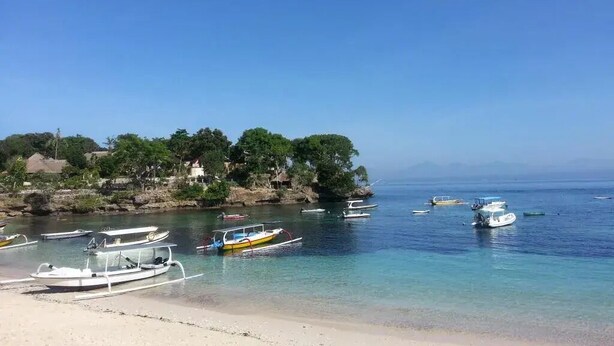 A beach with boats docked near the shore and a forested area in the background. - D'yuki Huts Lembongan (Lembongan Island)