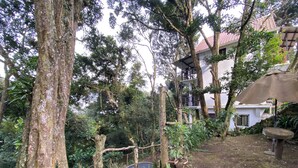 Um jardim com árvores grandes, um edifício branco com telhado vermelho e um banco de pedra.