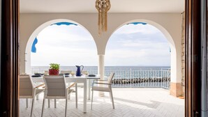 Ein Essbereich im Freien mit Blick auf das Meer, ausgestattet mit einem Tisch, Stühlen, einem Topfpflanzen und einer Karaffe.