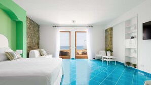 Ein Hotelzimmer mit einem Bett, einem kleinen Tisch, einem Sessel, einem Fernseher und Blick auf den Strand durch die Tür.