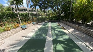 Een jeu de boules baan, omringd door een tegelpad en weelderige begroeiing.