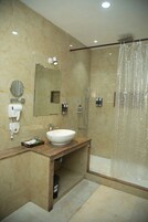 Un baño moderno con tocador de mármol, un espejo grande, lavabo empotrado, cabezal de ducha de mano y ducha con mampara de vidrio.