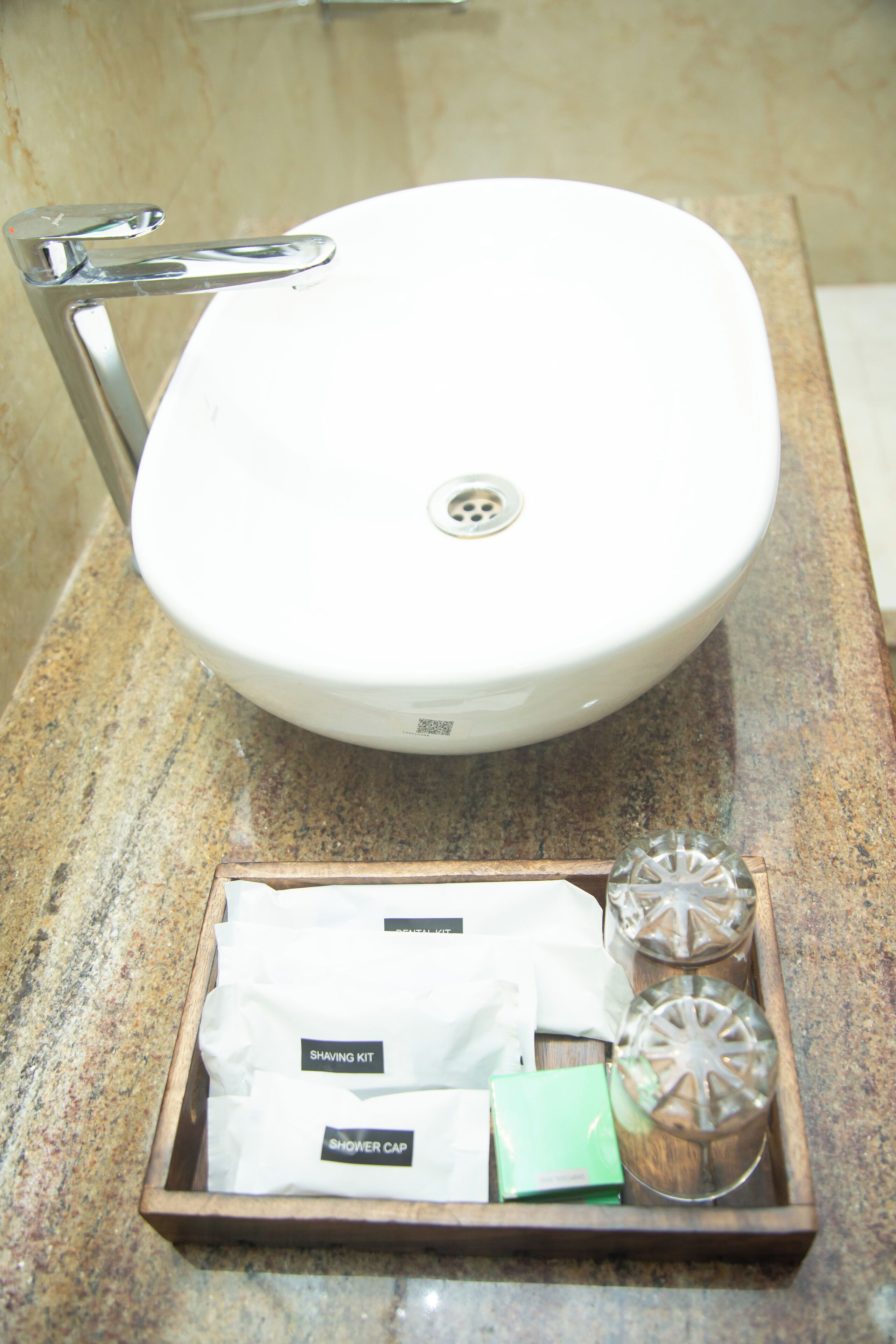 Un lavabo de salle de bain avec un robinet chromé, un plateau en bois contenant un kit de rasage, un bonnet de douche et deux récipients en verre.