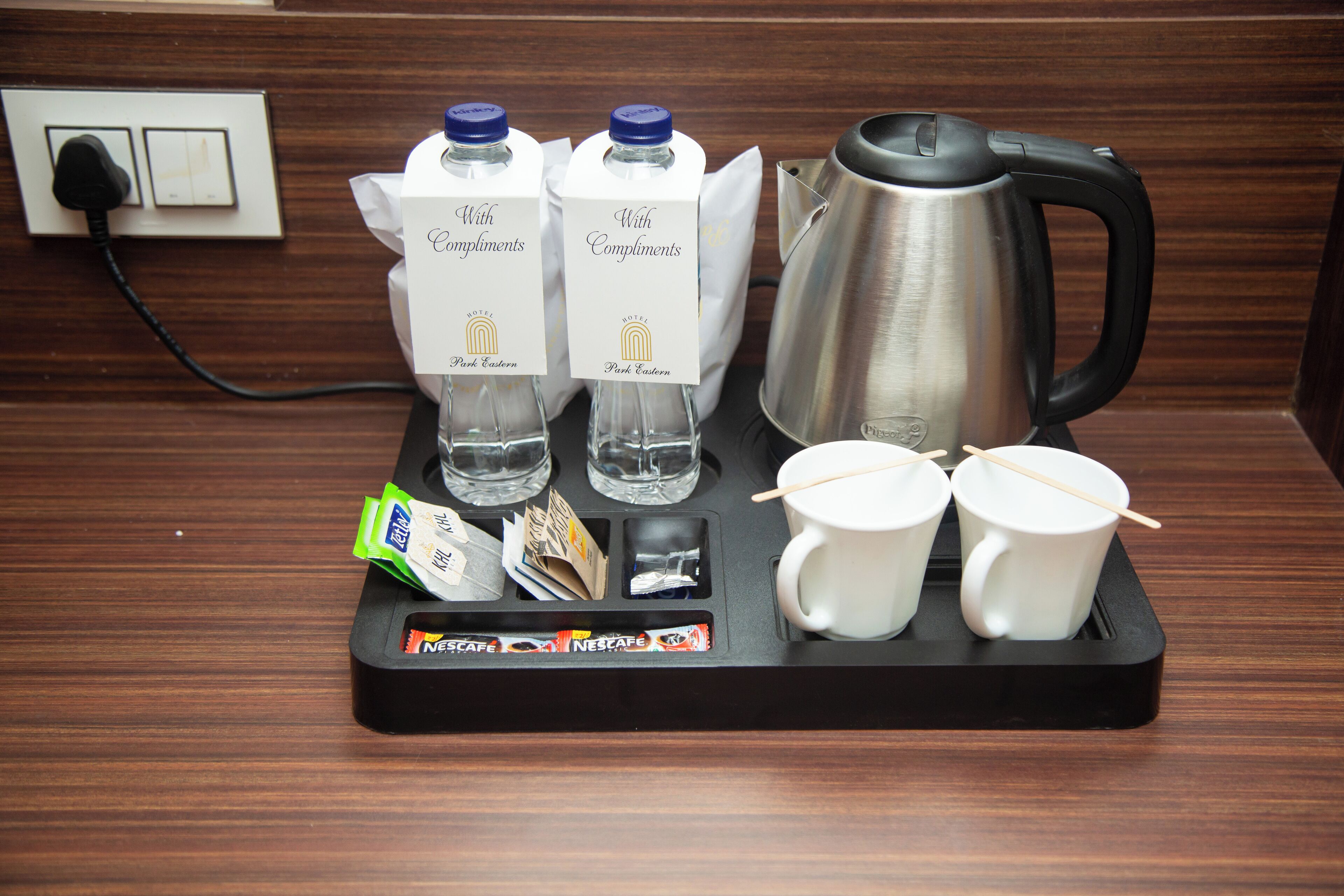 Un plateau de petit-déjeuner dans une chambre d’hôtel, avec une machine à café, deux bouteilles d’eau, deux tasses et quelques aliments pour le petit-déjeuner.