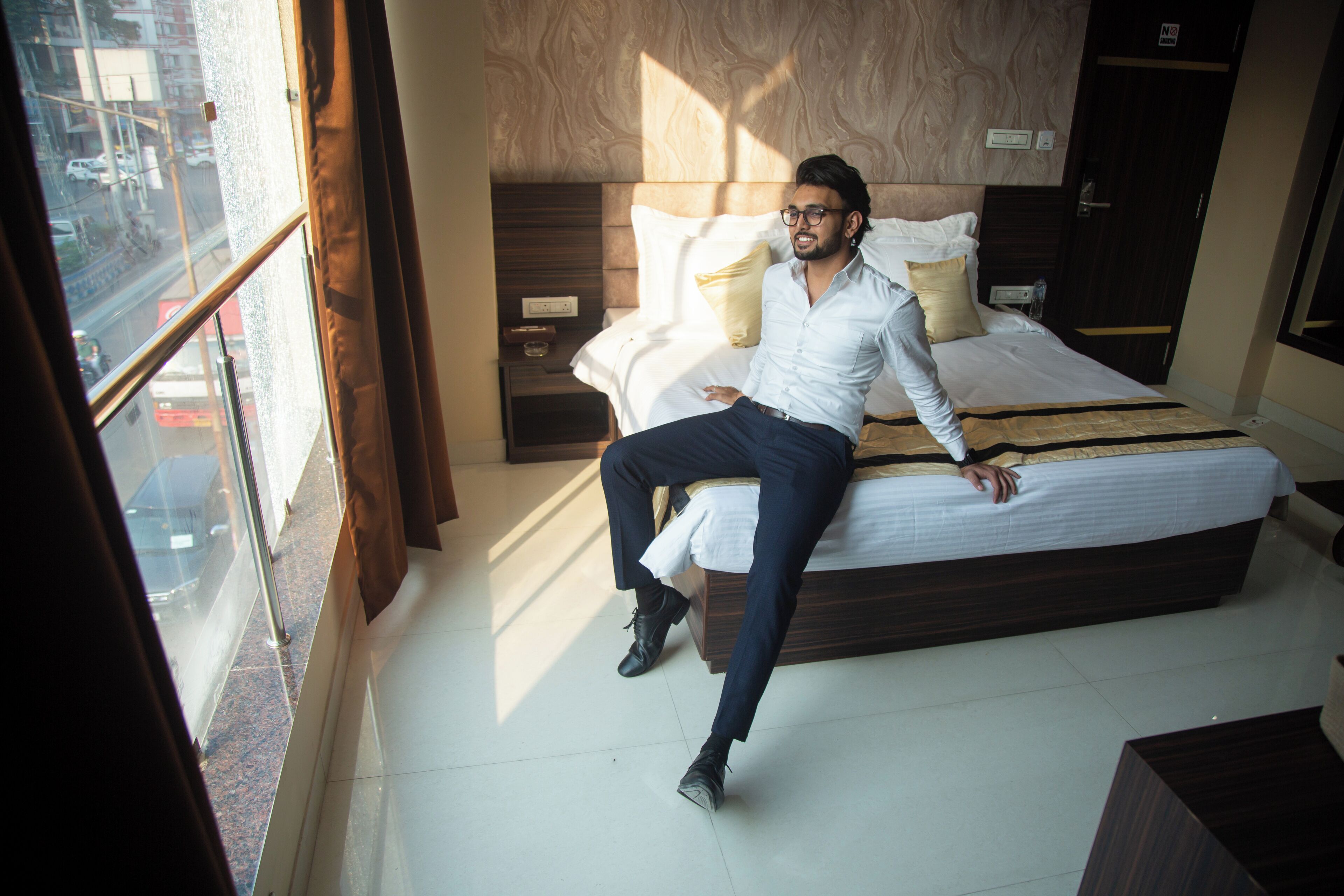 A modern hotel room with a large bed, a nightstand, and a window with a view of the street.