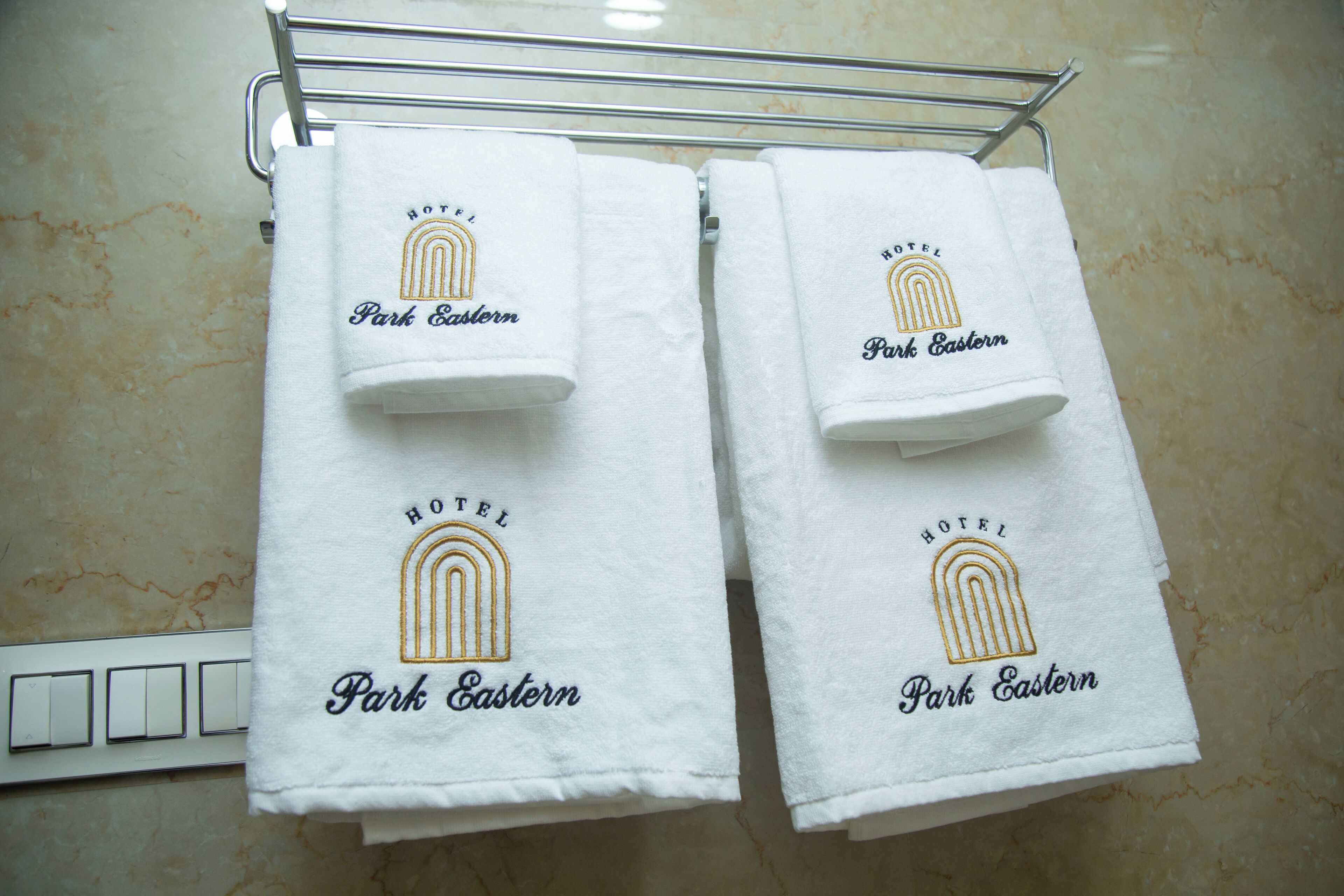 Two white towels hanging on a metal rack with the text "HOTEL Park Eastern" and a stylized hotel logo.