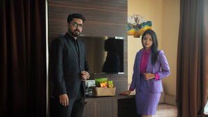 A man and a woman standing in a modern hotel room with a TV, a small table with snacks, and a sofa. - PARK EASTERN HOTEL (Kolkata)