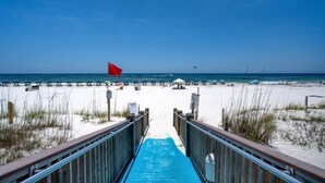 A beach with a wooden walkway leading to the water, a red flag, and a clear blue sky. - Summerchase 307 by Liquid Life (Orange Beach)