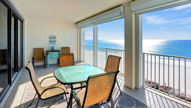 A balcony with a glass table and chairs, overlooking a beach. - Windward Pointe 805 by Liquid Life (Orange Beach)