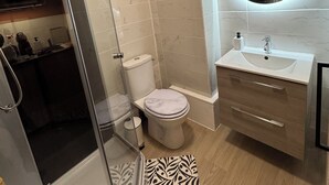 Un baño con ducha envuelta en vidrio, inodoro, lavamanos con espejo y una alfombra estampada.